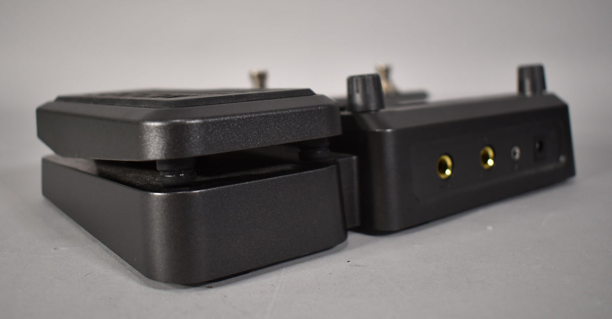A dark gray multi-effects pedal, viewed from the side, showing the expression pedal and two gold-colored input jacks.