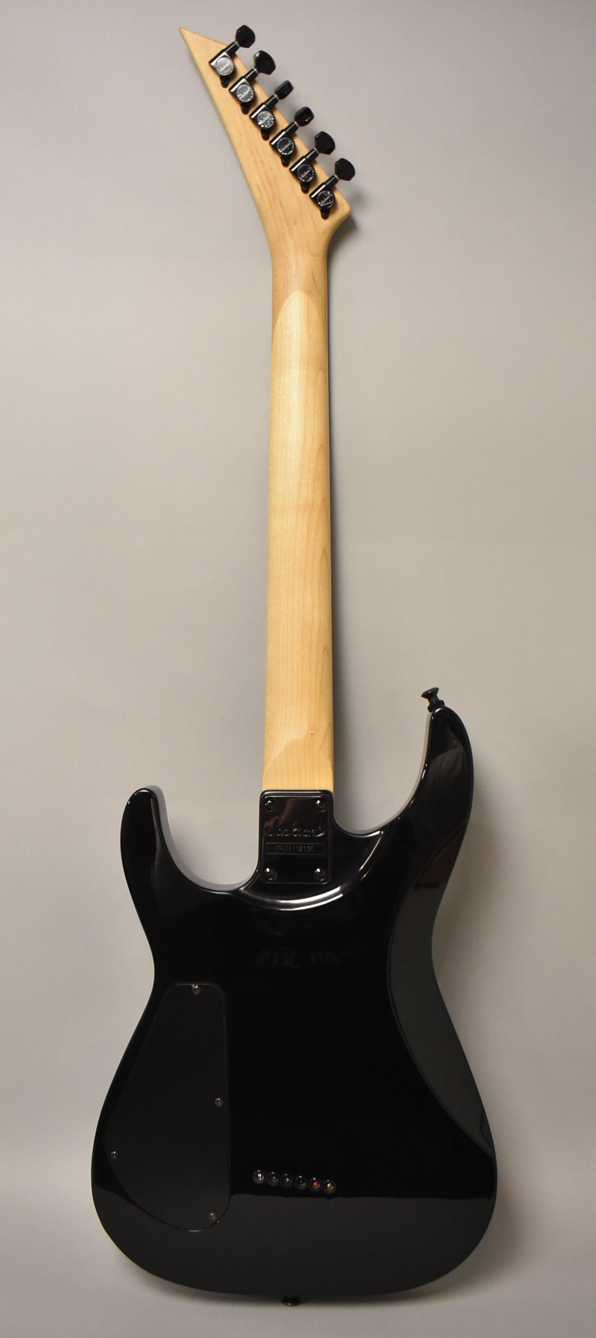 The back of a black gloss electric guitar, showing its light wood neck, pointed headstock with black tuners, and string-through-body ferrules.