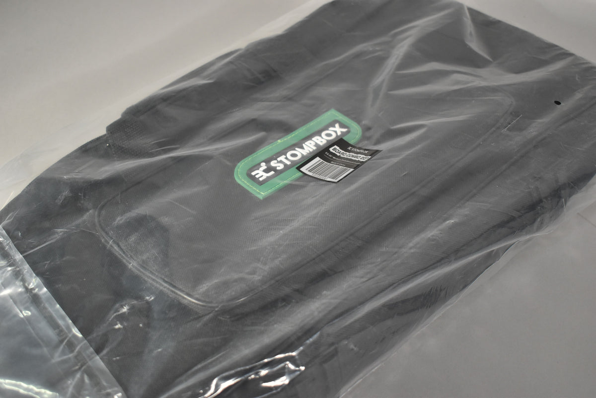 The black carrying bag is shown from above, still sealed in clear plastic, with a green "STOMPBOX" tag visible.