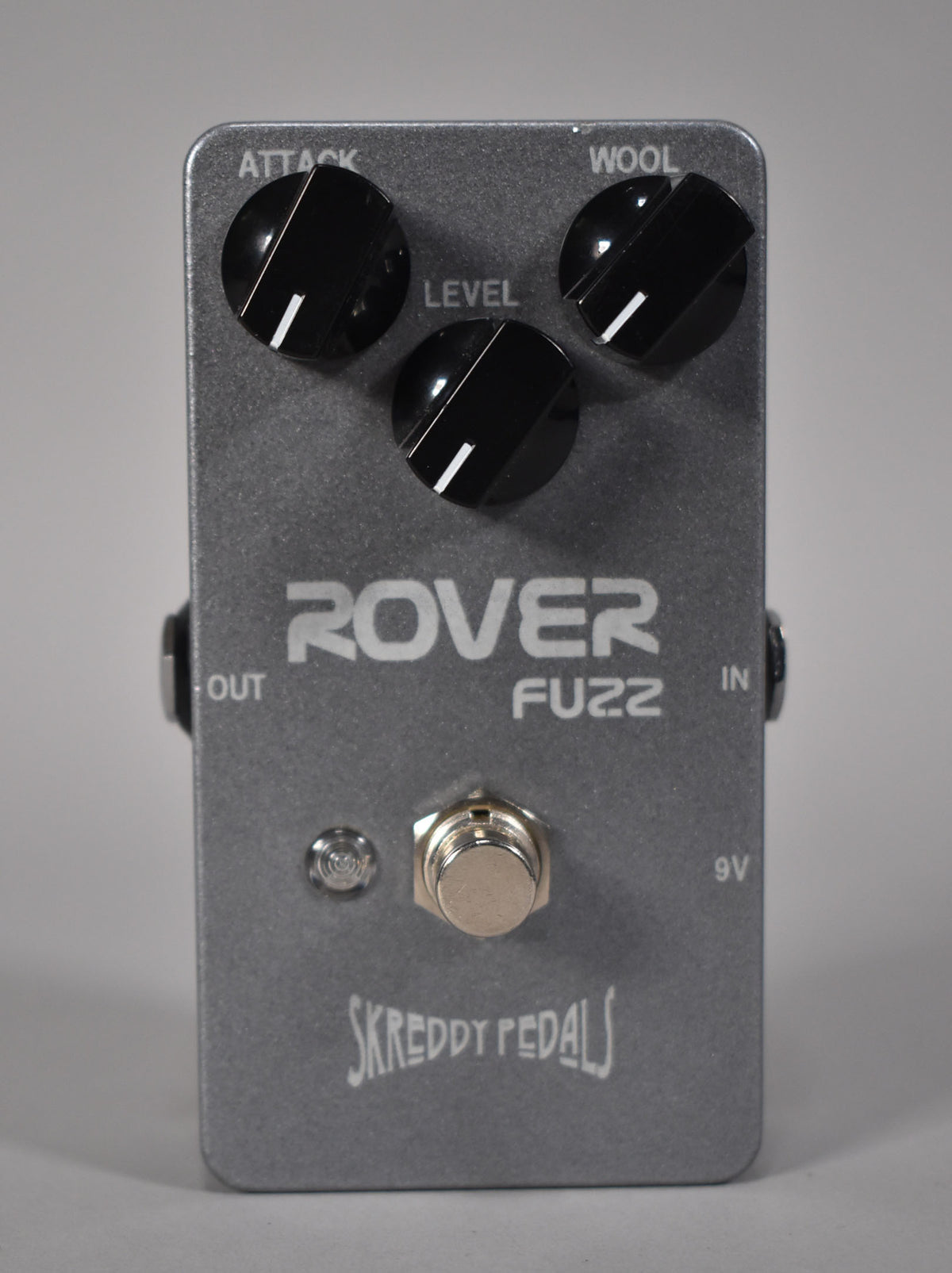 A top-down view of a rectangular, dark grey fuzz pedal with three black control knobs and a silver footswitch.