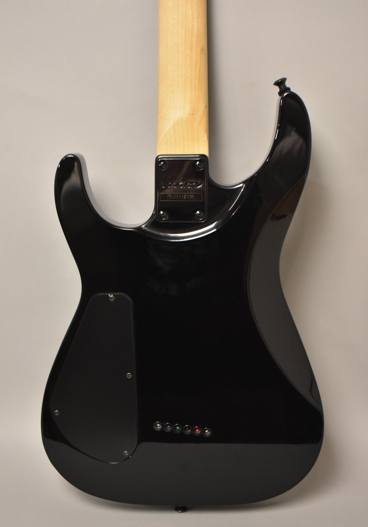 The back of a black electric guitar with a light wood neck, showing a control cavity cover and six string-through-body ferrules.