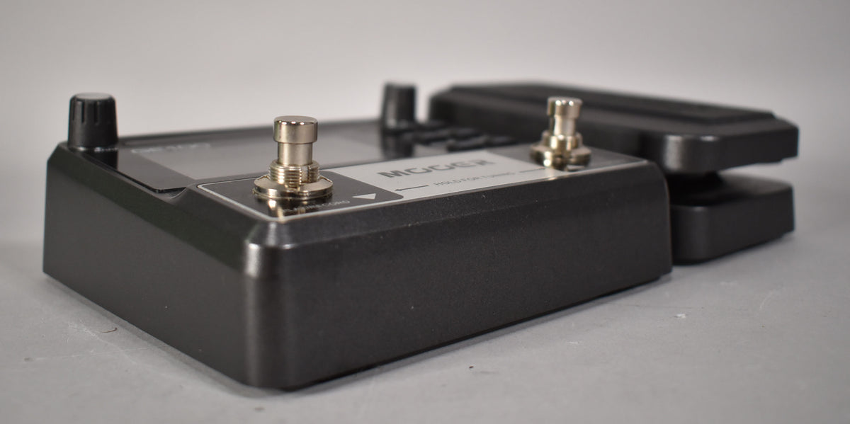 A dark grey multi-effects pedal, viewed from the right side, showing two silver footswitches and a black control knob.