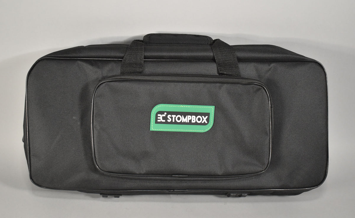 A black fabric carrying bag for a pedalboard, viewed from above, with a green rectangular logo on the front pocket.