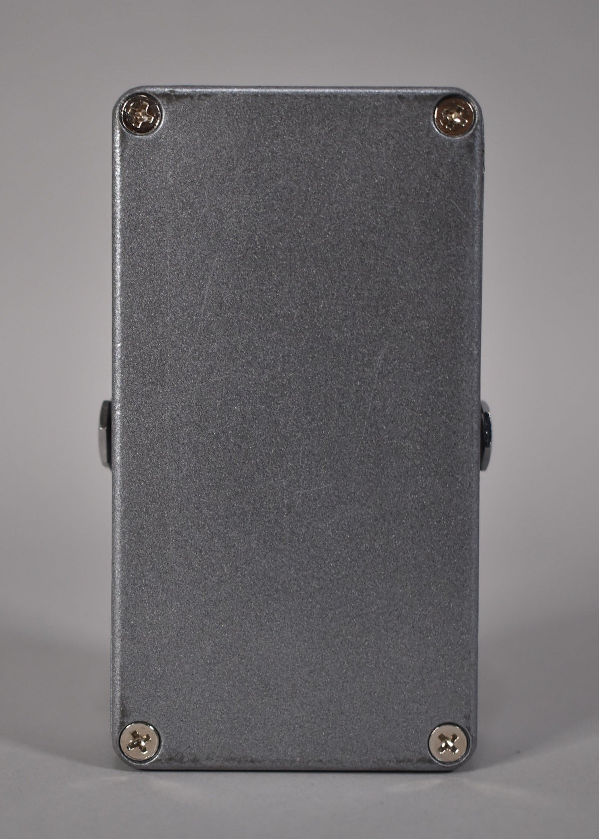 The bottom of the gray, textured pedal, showing four silver Phillips head screws and slight wear on the finish.