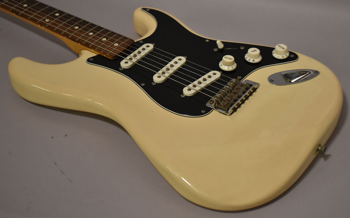 The Arctic White Stratocaster body, with a black pickguard and white pickups, is angled from the lower right, showing the bridge and controls.