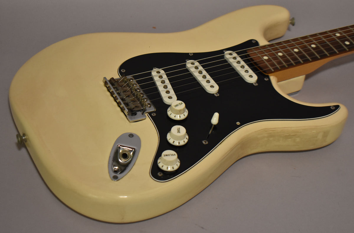 The Arctic White Stratocaster body, angled from the lower bout, shows a black pickguard, three single-coil pickups, and cream control knobs.