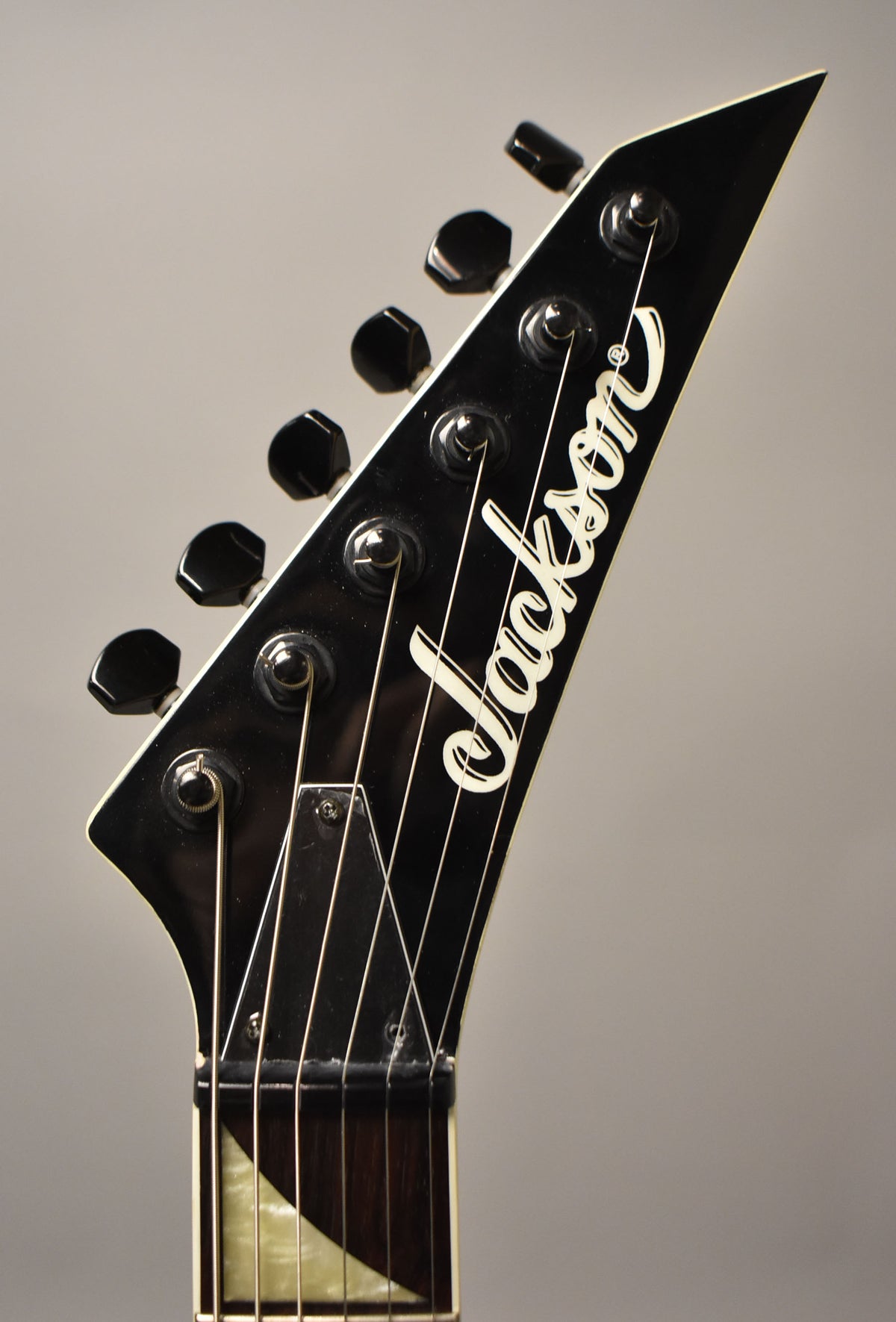 Close-up, angled view of the glossy black headstock with white binding, showing six black tuners and the top of the fretboard.