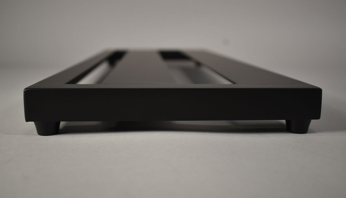 The black pedalboard is viewed from the side, showing its low profile and four rubber feet.