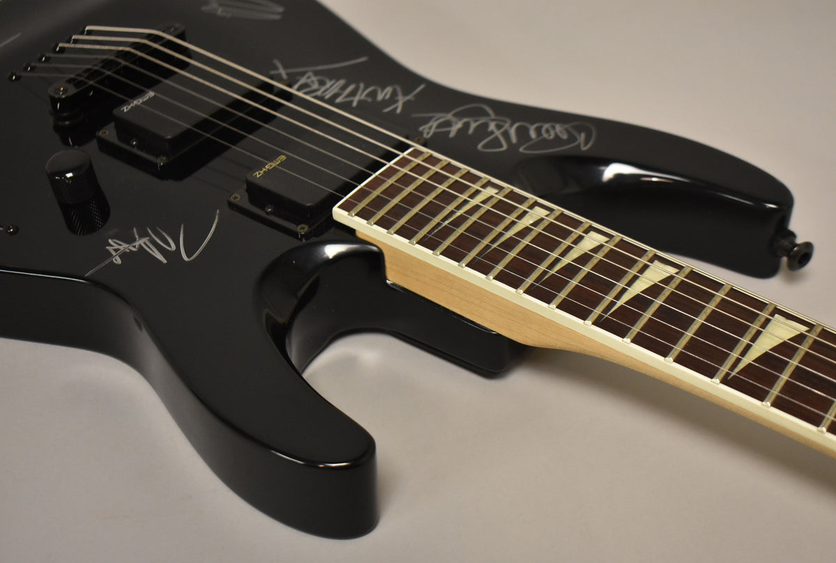 The black electric guitar's body, with visible signatures, angles toward the neck with sharkfin inlays on a dark fretboard.