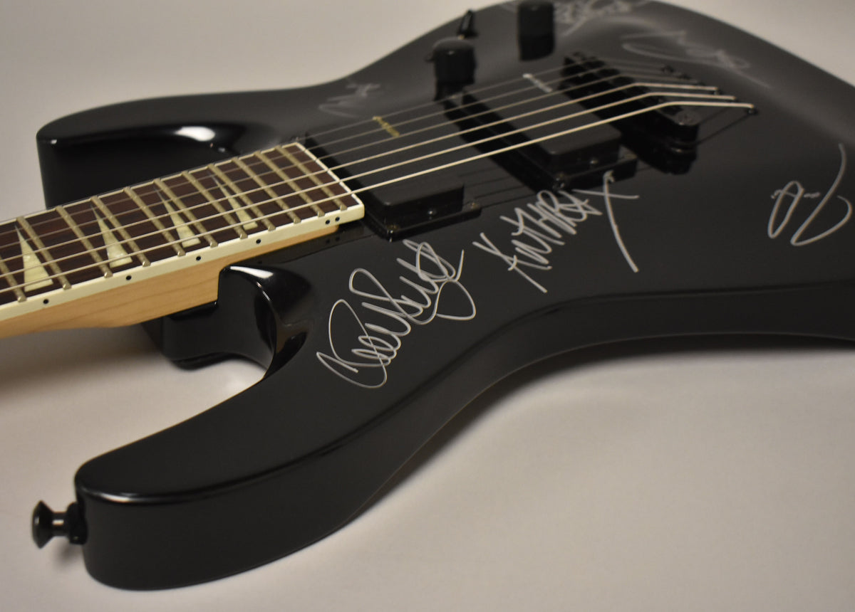Gloss black electric guitar body with white signatures, two humbuckers, and a maple neck with sharkfin inlays.
