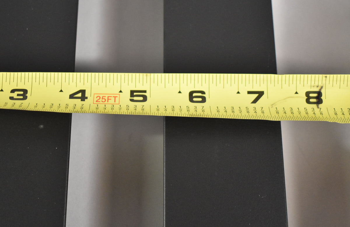 A yellow tape measure, showing inches 3 through 8, lies across the matte black pedalboard slats, indicating their width.