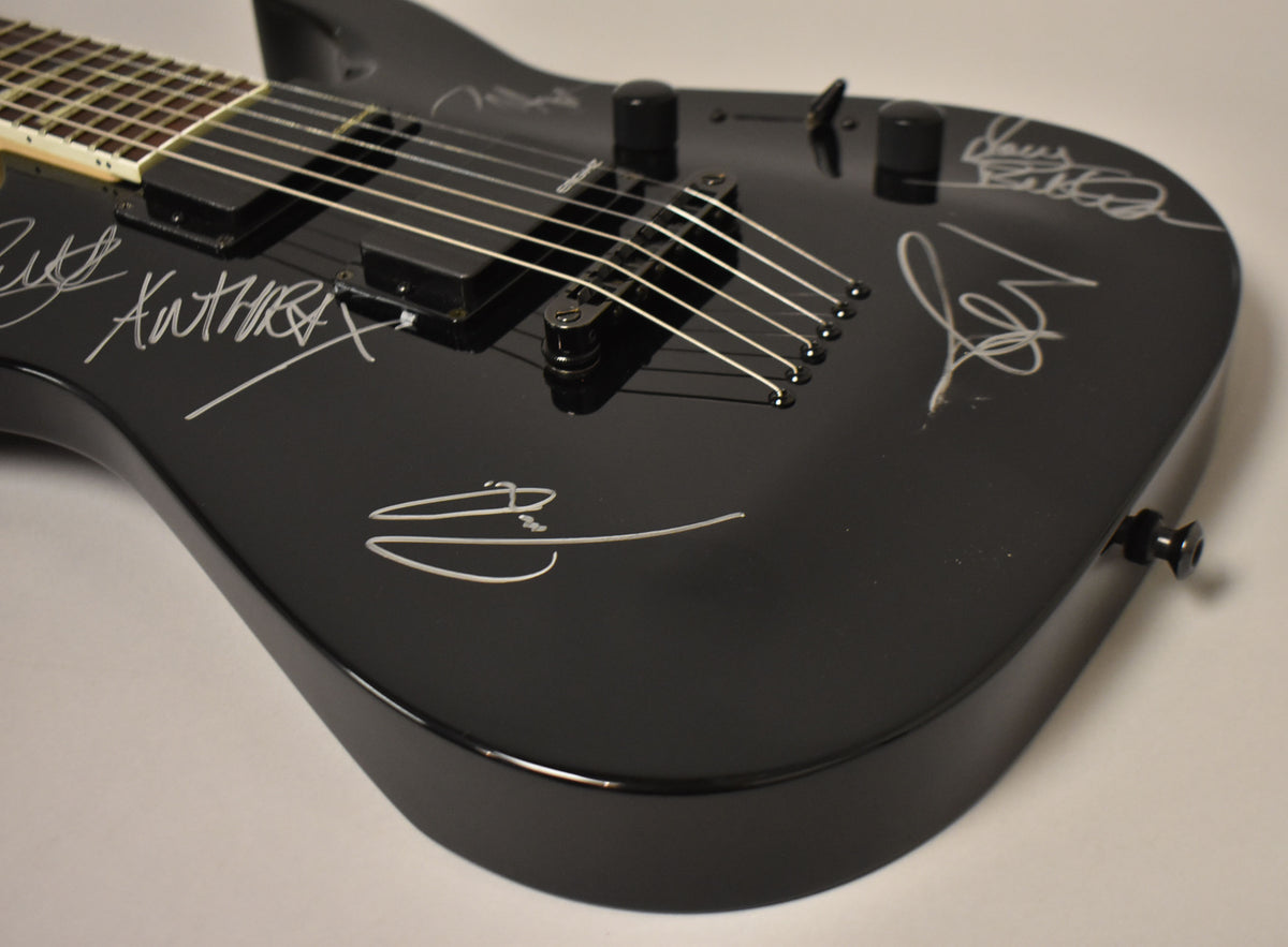 Close-up of the glossy black guitar body, angled from the lower bout, showing white signatures, black humbuckers, and a fixed bridge.