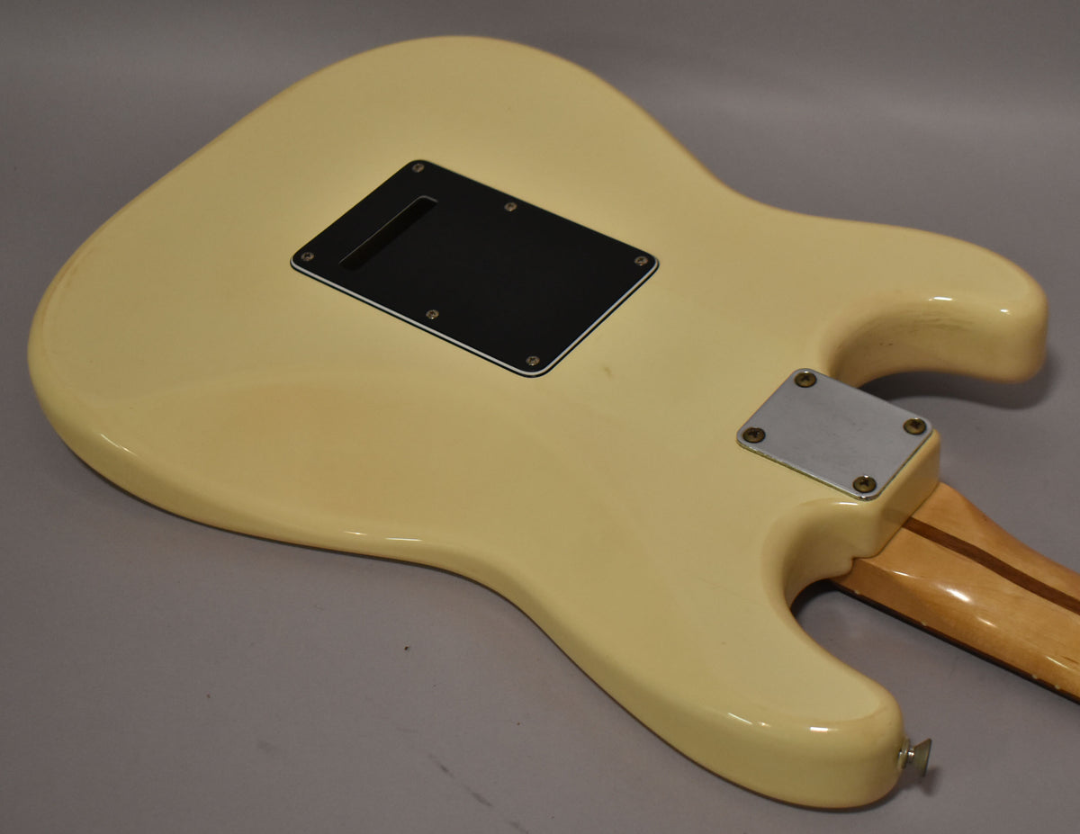 The back of an off-white Stratocaster body with a black tremolo cover and a silver neck plate, showing light wear.