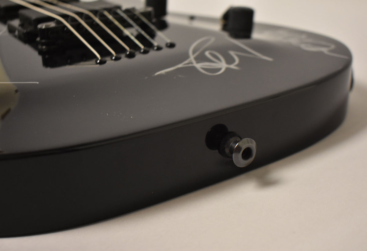 Close-up of the guitar's lower bout, showing the black gloss finish, output jack, and a white signature on the body.