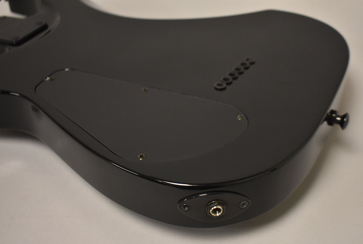 The guitar's black matte back shows a control cavity cover, string-through ferrules, and a glossy output jack on the lower bout.