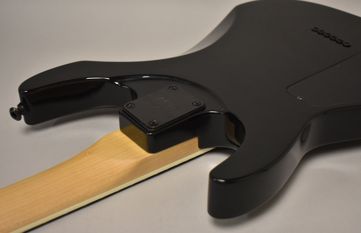 The guitar's glossy black body and neck joint are visible from the back, with a light maple neck and black neck plate.