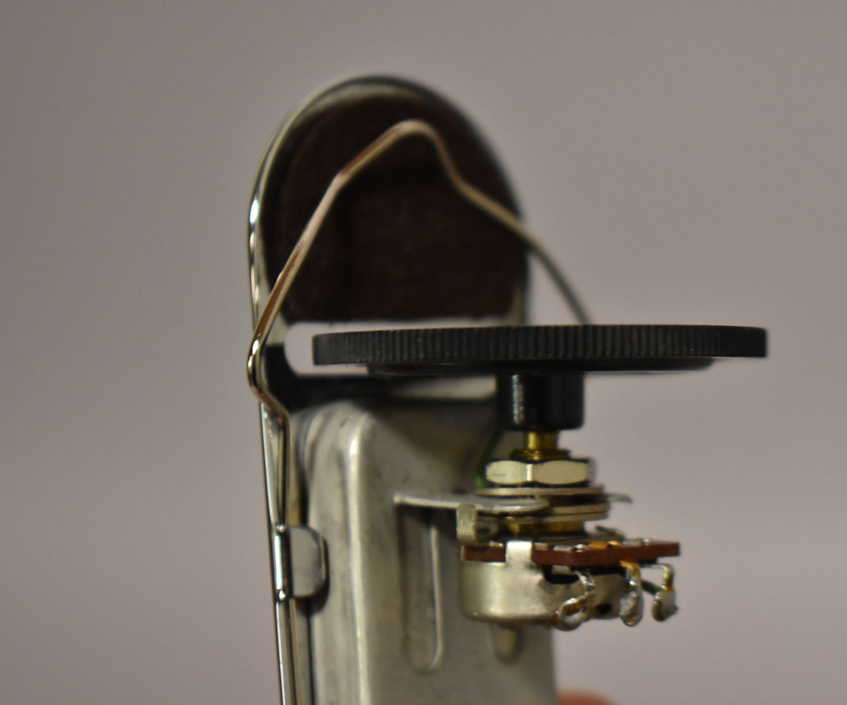 Close-up of the chrome pickup's side, showing a black ridged control knob and the potentiometer's exposed solder lugs.