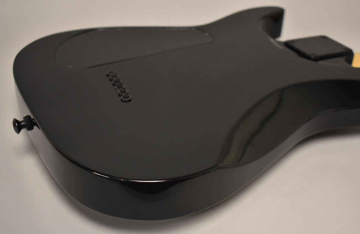 The guitar's glossy black back is angled, showing the string-through ferrules, control cavity cover, and a black strap button.