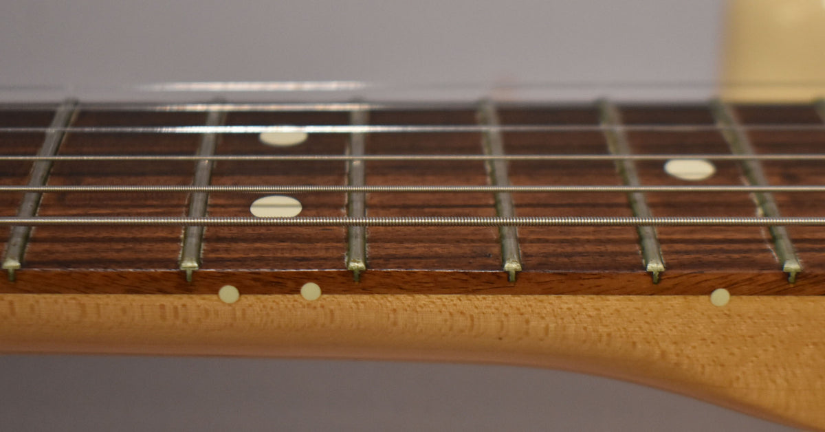 Close-up of the rosewood fretboard and maple neck, showing light wear on the frets and side dots.