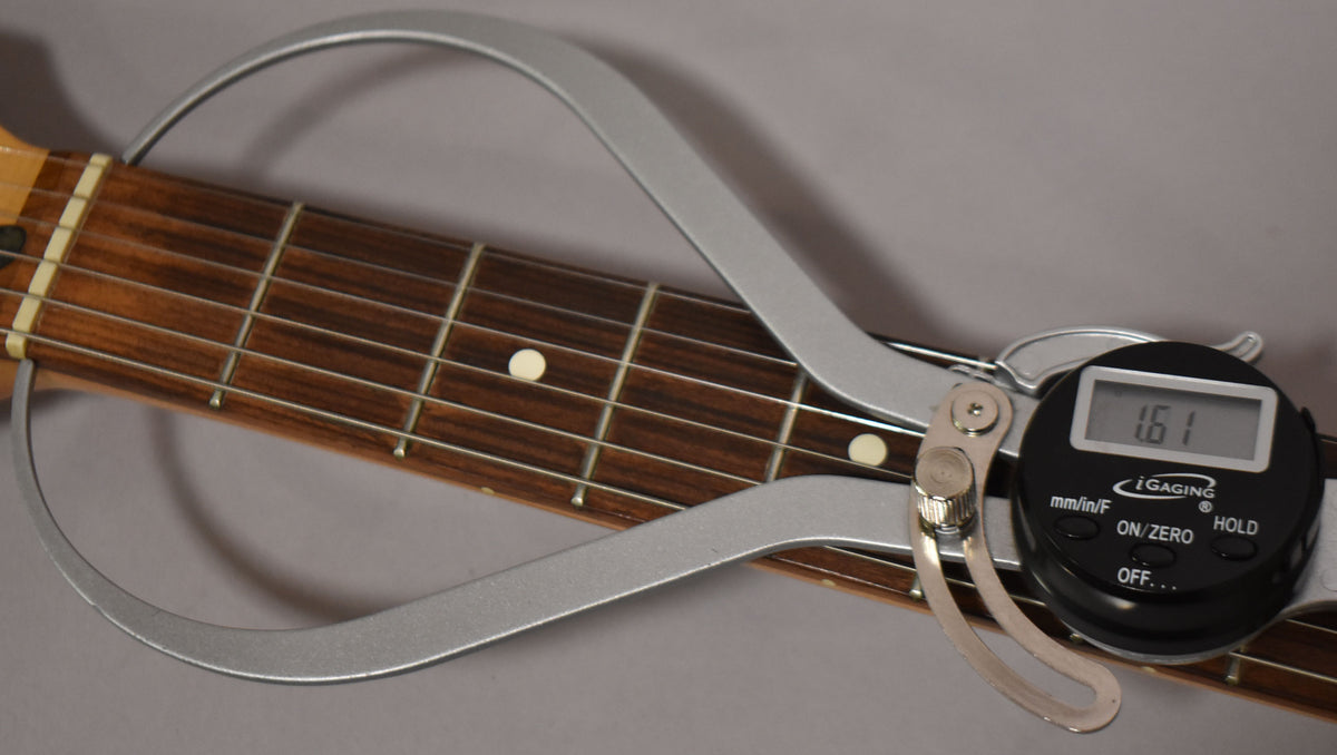 A digital caliper measures the guitar's dark rosewood fretboard, showing a 1.61-inch nut width.