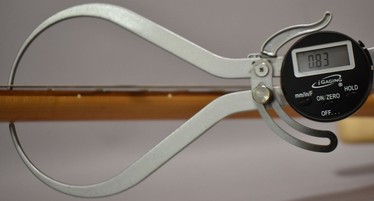A digital caliper measures the string height at the 12th fret, showing a reading of 0.83mm above the light brown fretboard.