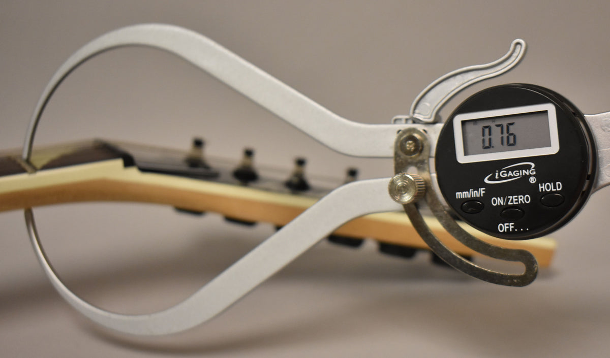 A digital caliper measures the neck thickness at the first fret, displaying "0.76" on its screen.