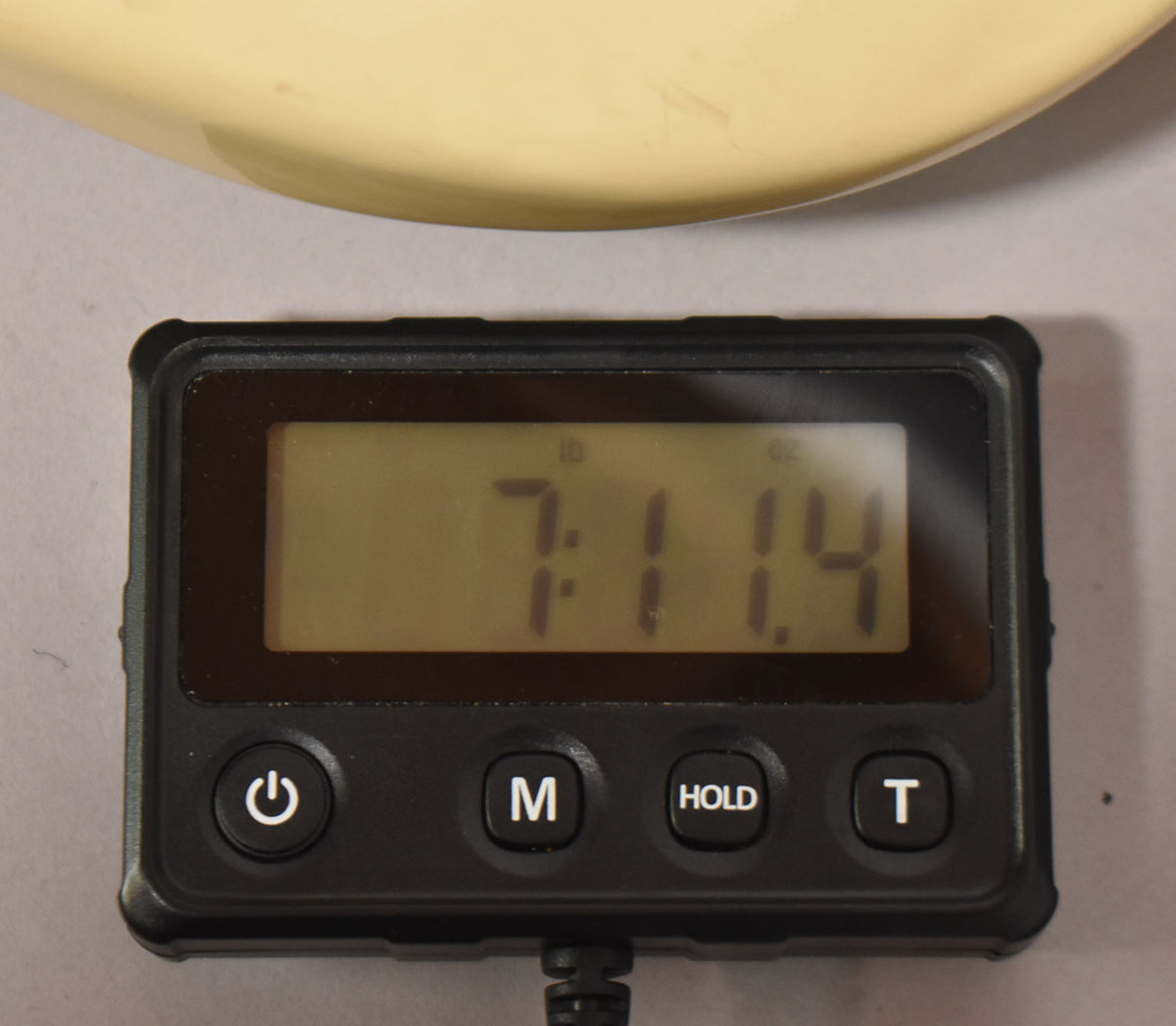 Close-up of a digital scale showing "7:1.4" (7 pounds, 1.4 ounces), with the guitar's aged white body visible above.