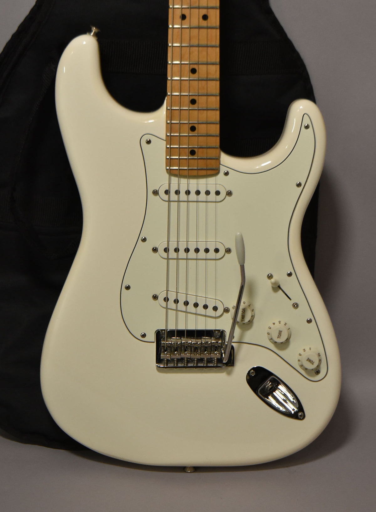 Full-frame view of a polar white Stratocaster with a maple neck, white pickguard, three single-coil pickups, and chrome hardware.