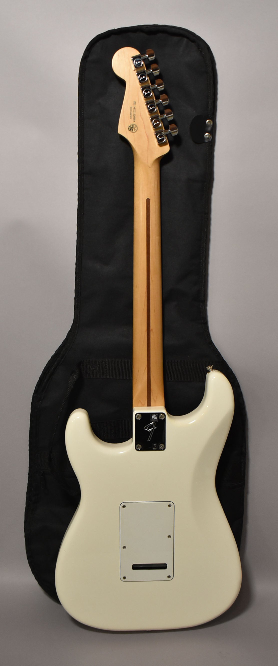 The back of a polar white Stratocaster with a maple neck, chrome tuners, and a white tremolo cover, resting in a black gig bag.