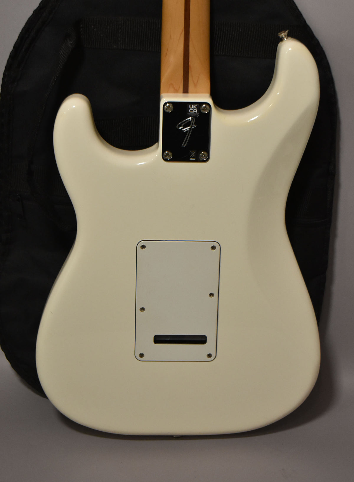 The back of a polar white Stratocaster, showing the neck plate, tremolo cover, and a light-colored wooden neck with a dark stripe.