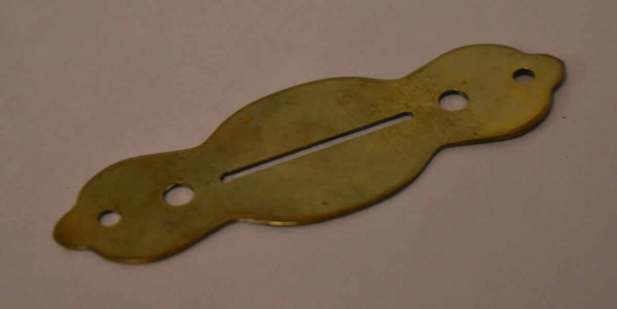 A gold brass selector switch plate, viewed from above, with a long slot and four screw holes, showing some tarnishing.