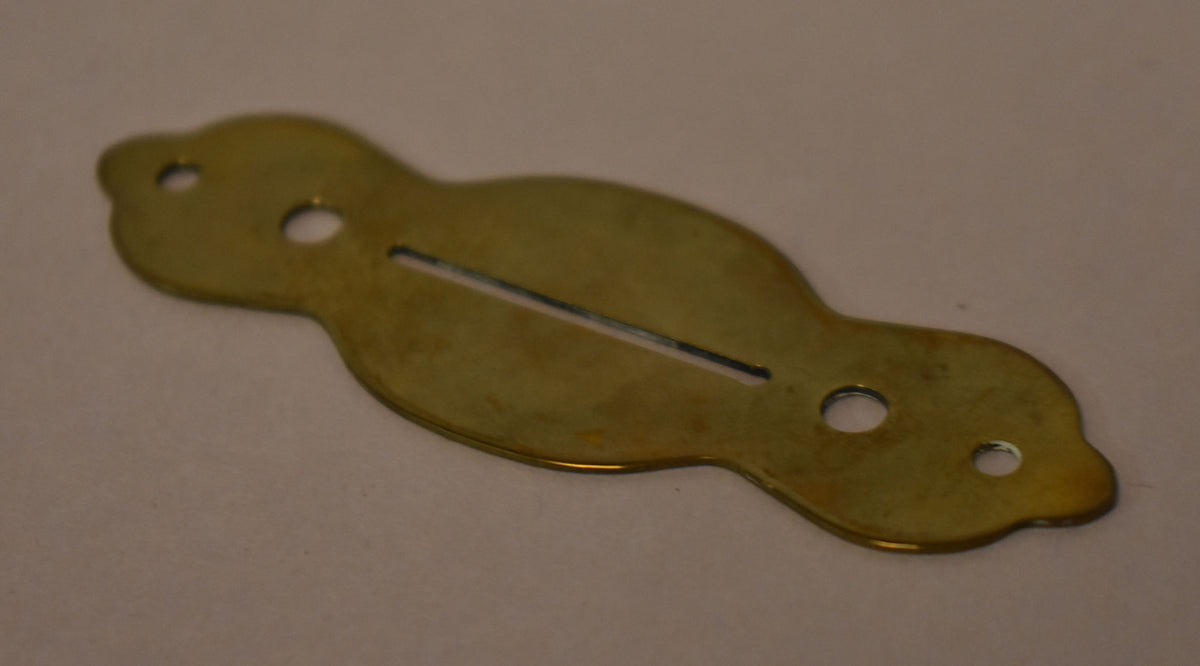 A gold brass selector switch plate, viewed from above, showing a long slot and three mounting holes, with some tarnishing.