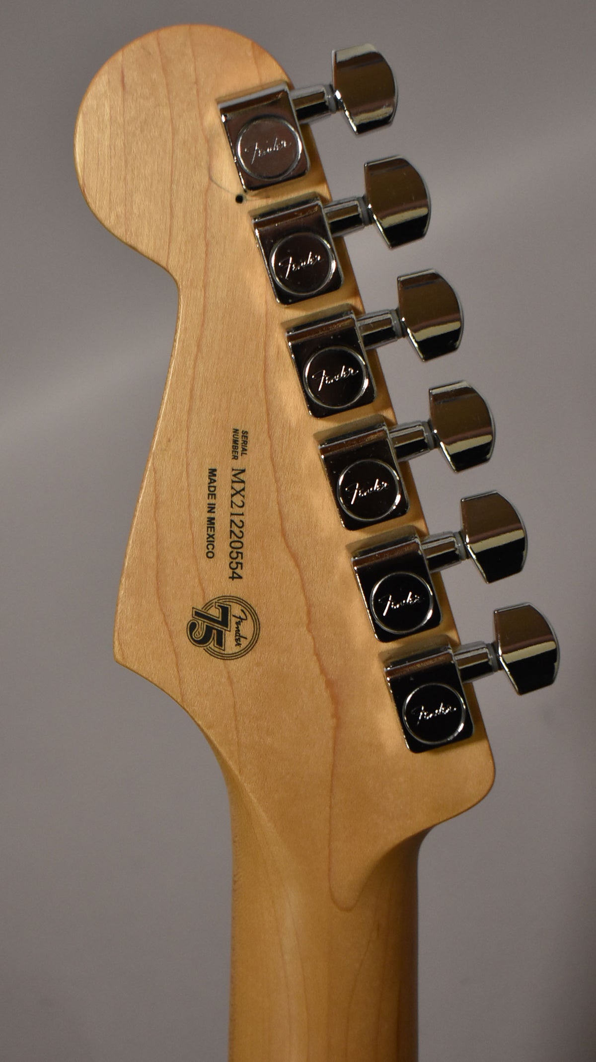 The back of a light wood headstock and neck, angled right, with six chrome tuning machines.