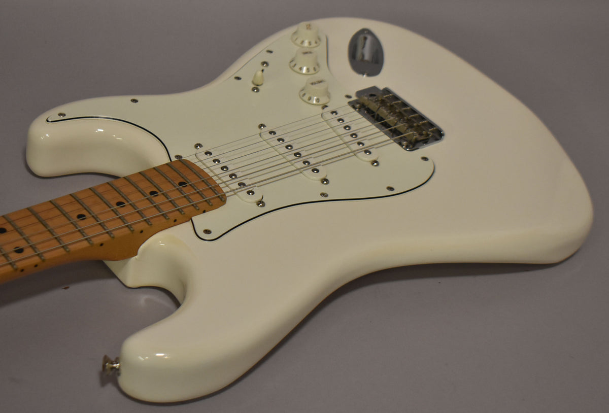 The polar white Stratocaster is angled from the left, showing its maple neck, white pickguard, three single-coil pickups, and chrome hardware.