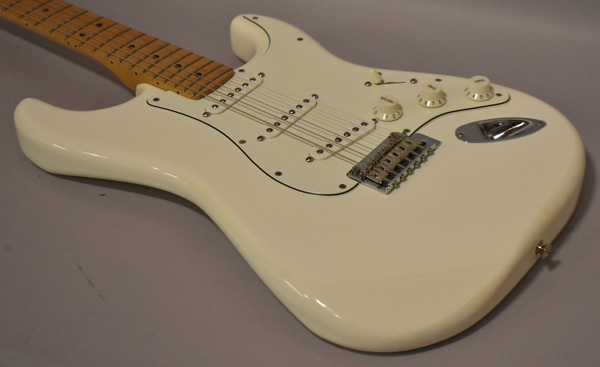The polar white Stratocaster is angled from the upper left, showing its glossy body, white pickguard, three single-coil pickups, and chrome hardware.