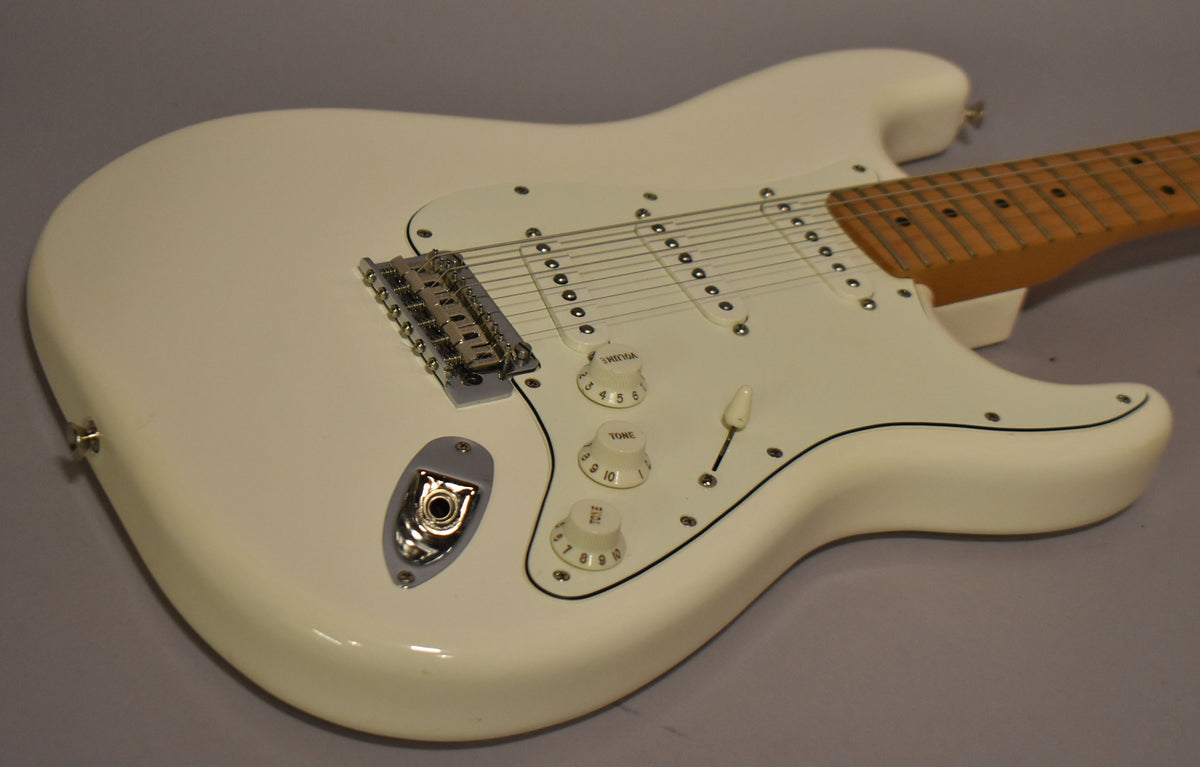 The polar white Stratocaster body is angled from the lower left, showing the white pickguard, three single-coil pickups, and chrome hardware.