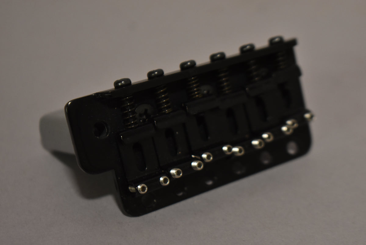 Black tremolo bridge viewed from an angle, showing six silver string saddles and six black intonation screws with springs.