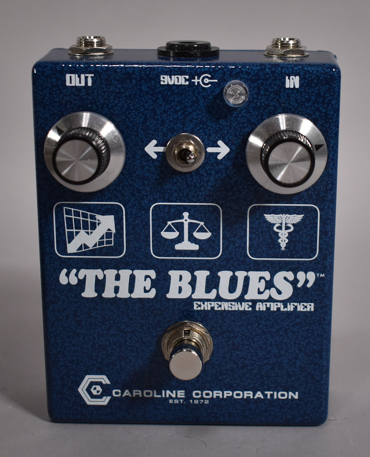 The blue textured pedal is viewed from the front, showing two large silver knobs, a toggle switch, and a footswitch.