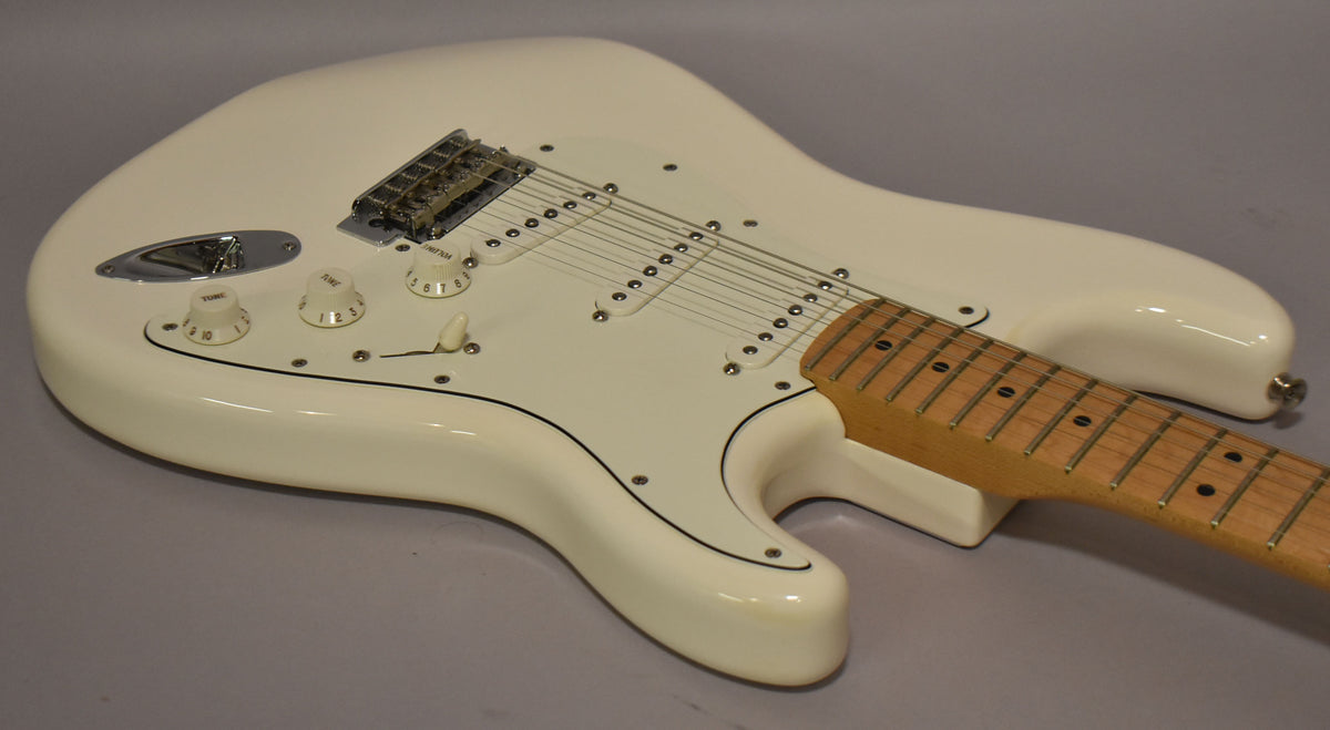 Polar white Stratocaster body, angled from above, showing the glossy finish, white pickguard, three single-coil pickups, and maple neck.