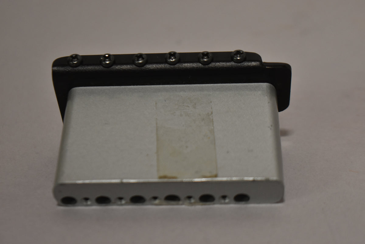 Side view of the black tremolo bridge with six silver saddle screws visible, and six string-through-body holes along the bottom edge.