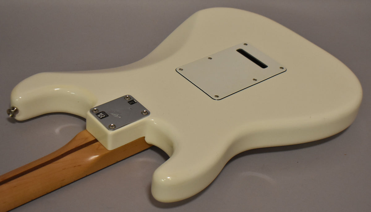 The back of a polar white Stratocaster, showing the neck plate, tremolo cavity cover, and a maple neck with a dark stripe.