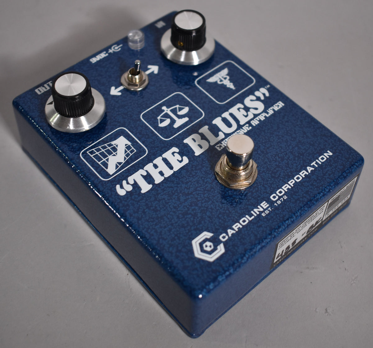 Top-down view of a metallic blue pedal with two silver knobs, a silver toggle switch, a clear LED, and a silver footswitch.