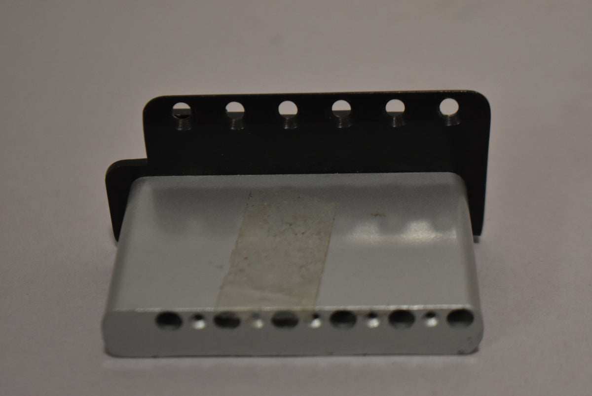 The black tremolo bridge base is seen from the side, revealing six string-through holes and six mounting holes along the top edge.