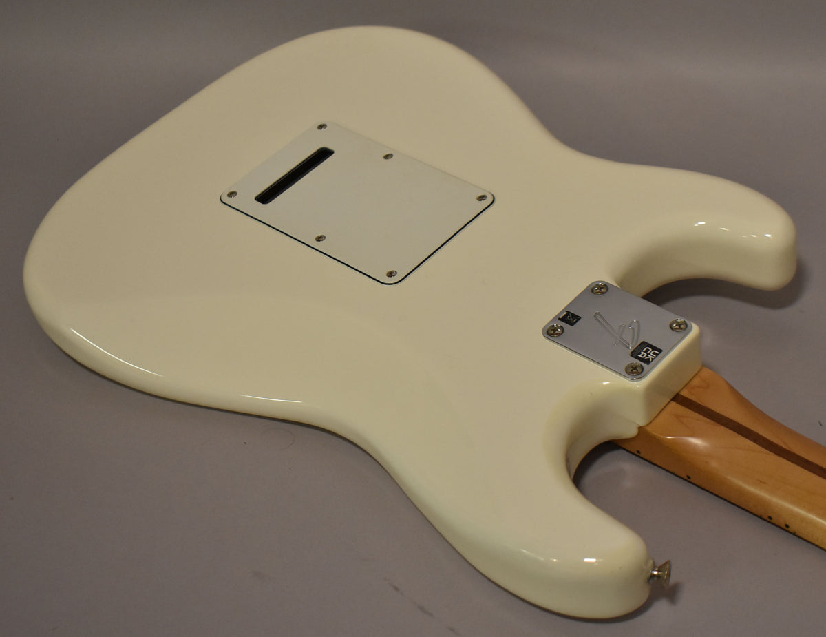 The back of a polar white Stratocaster body with a white tremolo cover, chrome neck plate, and light wood neck.