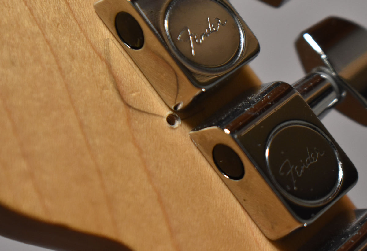Close-up of the light wood headstock and three chrome tuning pegs, with a string tree and string visible.