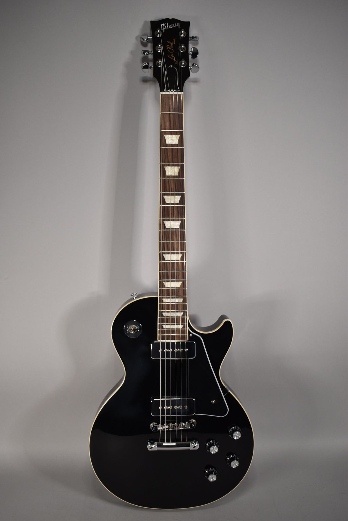 Full-length view of a glossy black Les Paul with cream binding, chrome hardware, two humbuckers, and four control knobs.