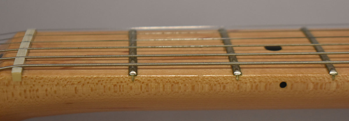 Close-up of the light wood fretboard and metal frets, showing the white nut and black dot inlays on the 3rd, 5th, and 7th frets.