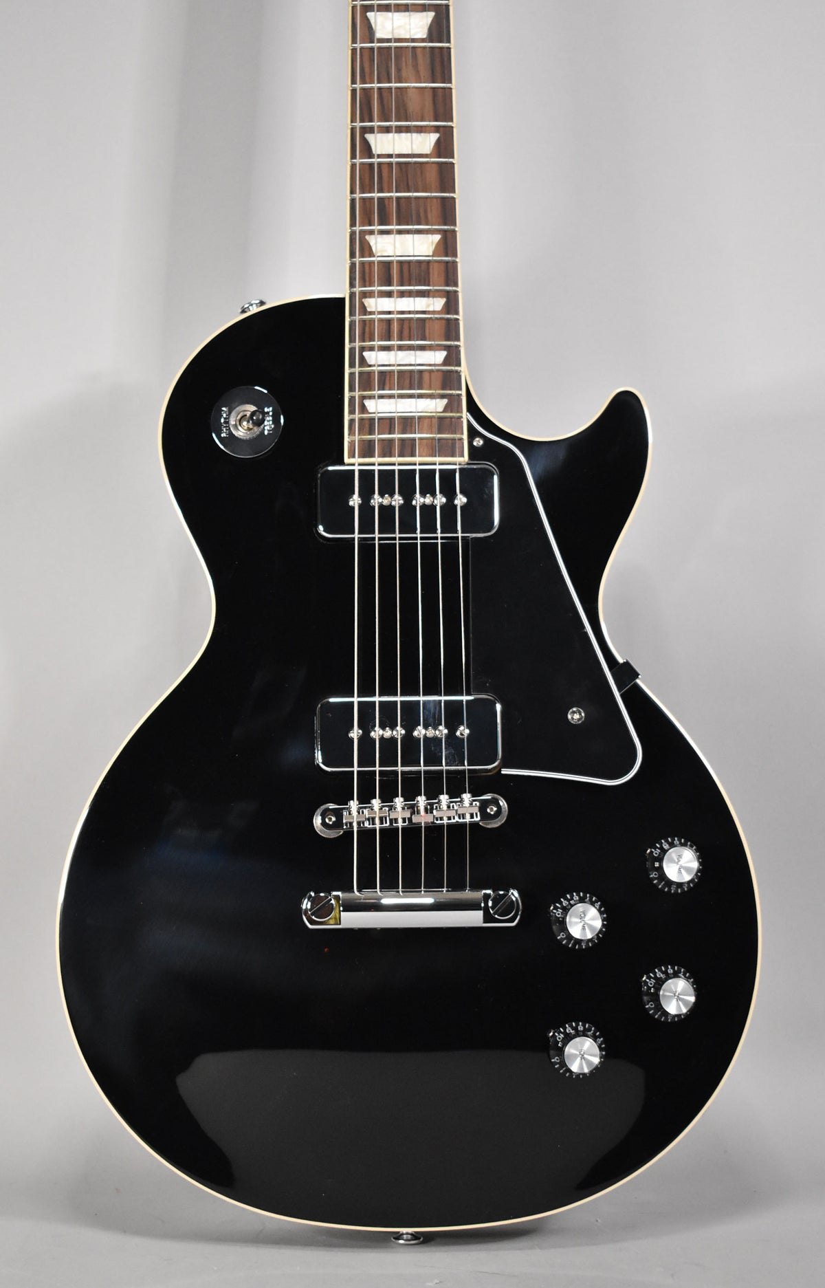 Full-frame, glossy black Les Paul with cream binding, two P90 pickups, a three-way toggle, and four chrome-capped knobs.