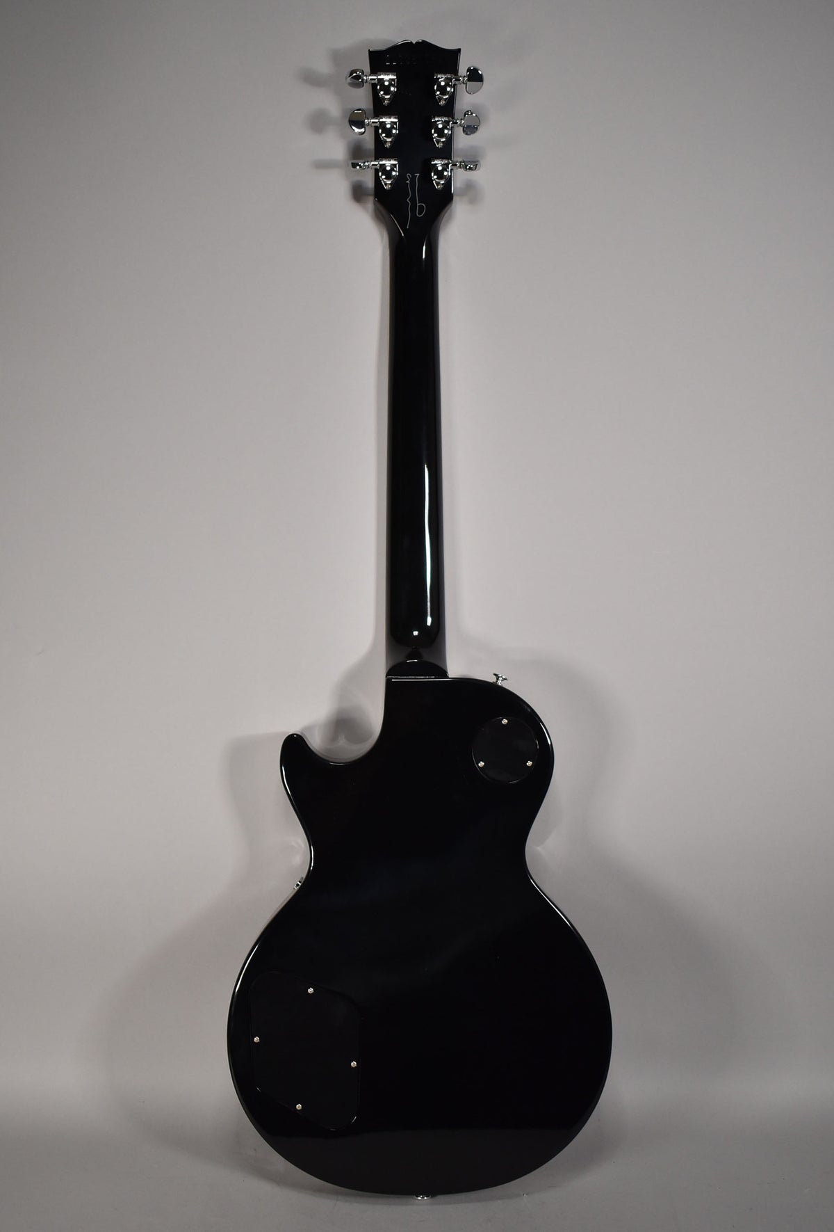 Full rear view of a glossy black Les Paul, showing the headstock with six chrome tuners and two control cavity covers.