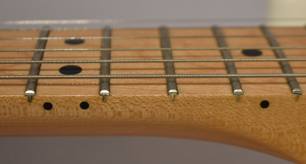 Close-up of the maple fretboard and frets, showing black dot inlays on the fretboard and side.